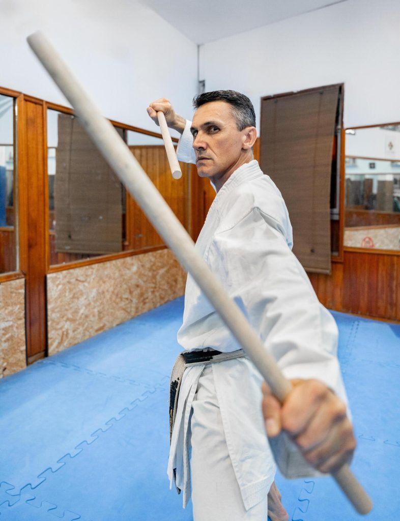 Karate practitioner with wooden training weapons - The Karate Shop Karate practitioner holding wooden training weapons in a dojo.
